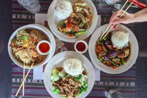 four PD Thai dishes arranged on a table with people eating them